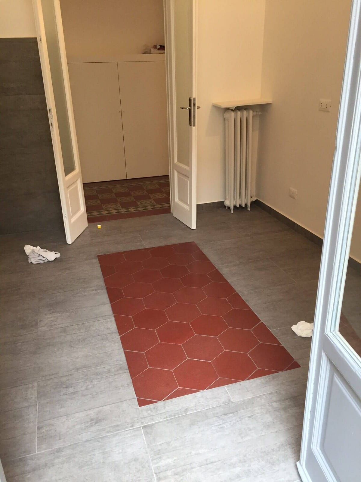 Pavimento effetto legno con inserto di piastrelle esagonali rosse davanti a una porta a vetri