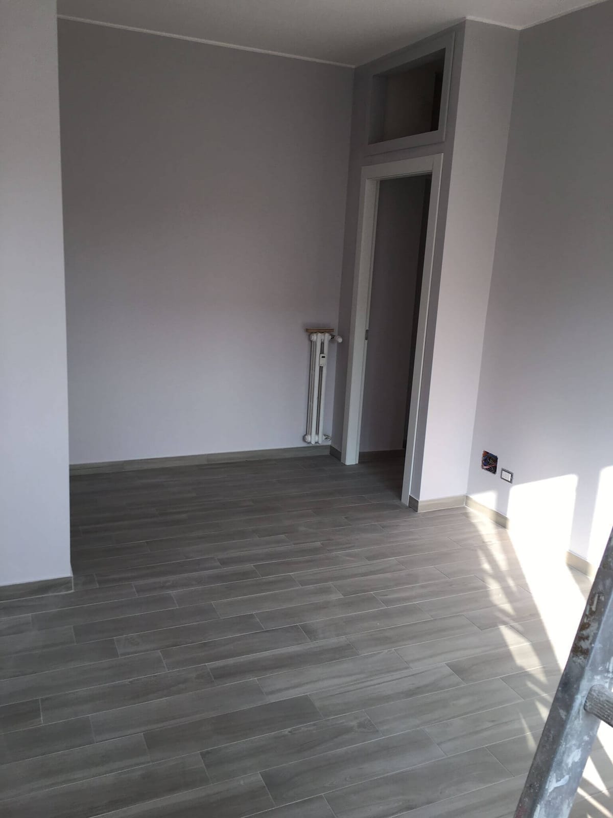 Stanza di un appartamento ristrutturato con pavimento in gres effetto legno e pareti tinteggiate
